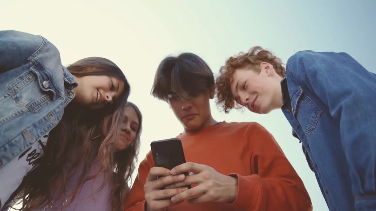 Eine Gruppe Von Teenagern Mit Zwei Mädchen Und Zwei Jungen Die Sich Etwas Lustiges Auf Dem Bildschirm Eines Mobiltelefons Ansehen