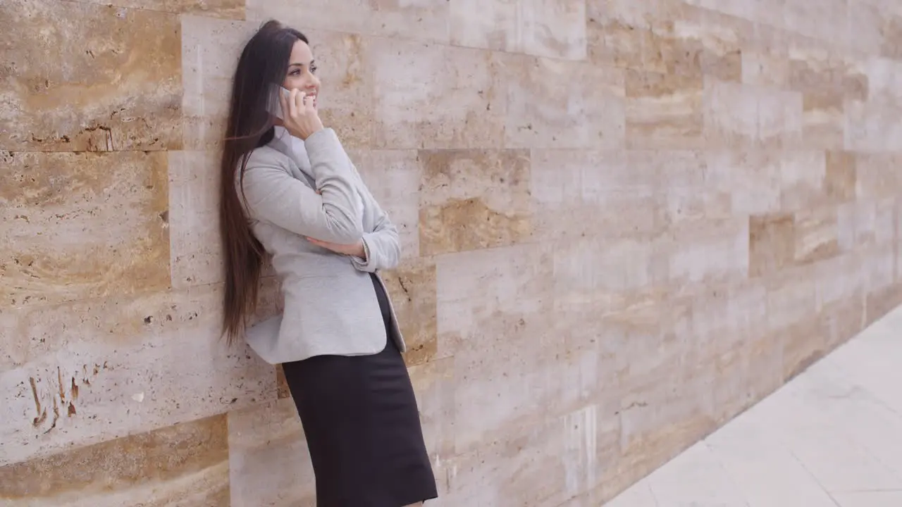 Happy woman talking on phone and leaning on wall