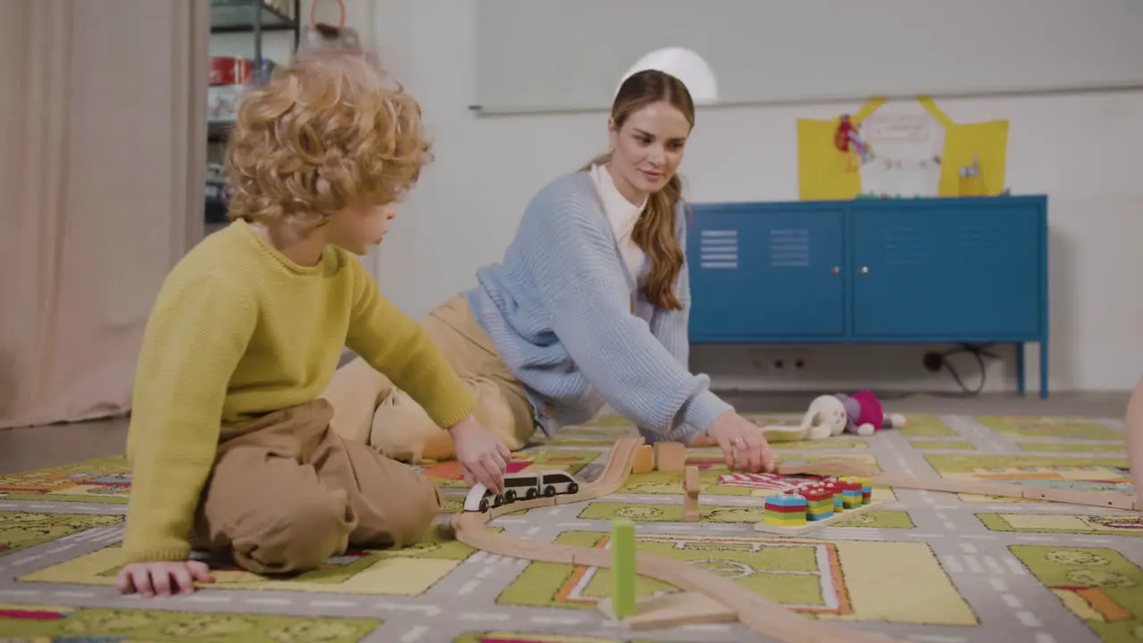 Der Kleine Blonde Junge Und Sein Lehrer Spielen Mit Holzautos Auf Dem Teppich Im Klassenzimmer Einer Montessori-Schule