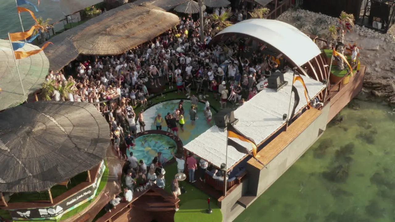 Multitud De Jóvenes Disfrutando De Su Tiempo En Una Ubicación De Club De Playa De Festival Tropical Diapositiva De Carro Aéreo A La Derecha