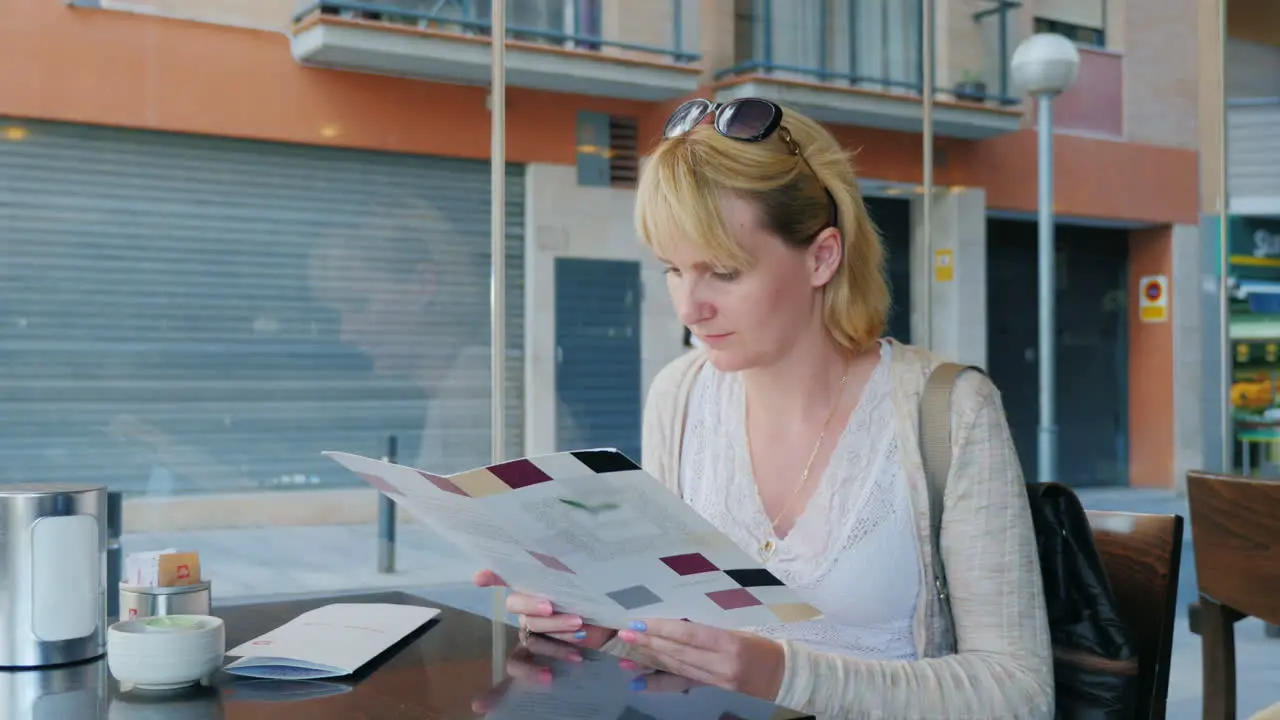 A young woman reads the menu in a cafe sits at a table by the window 1