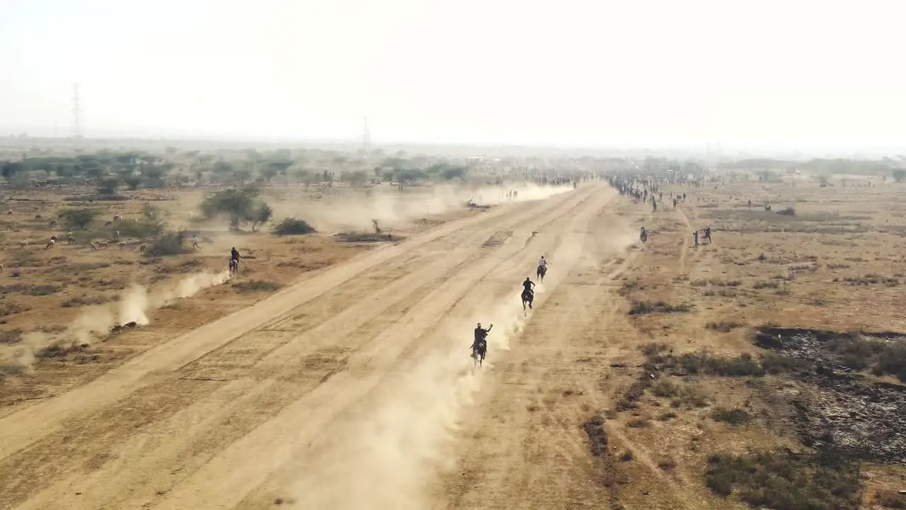 Aerial drone view of a horse race in a dusty field in India