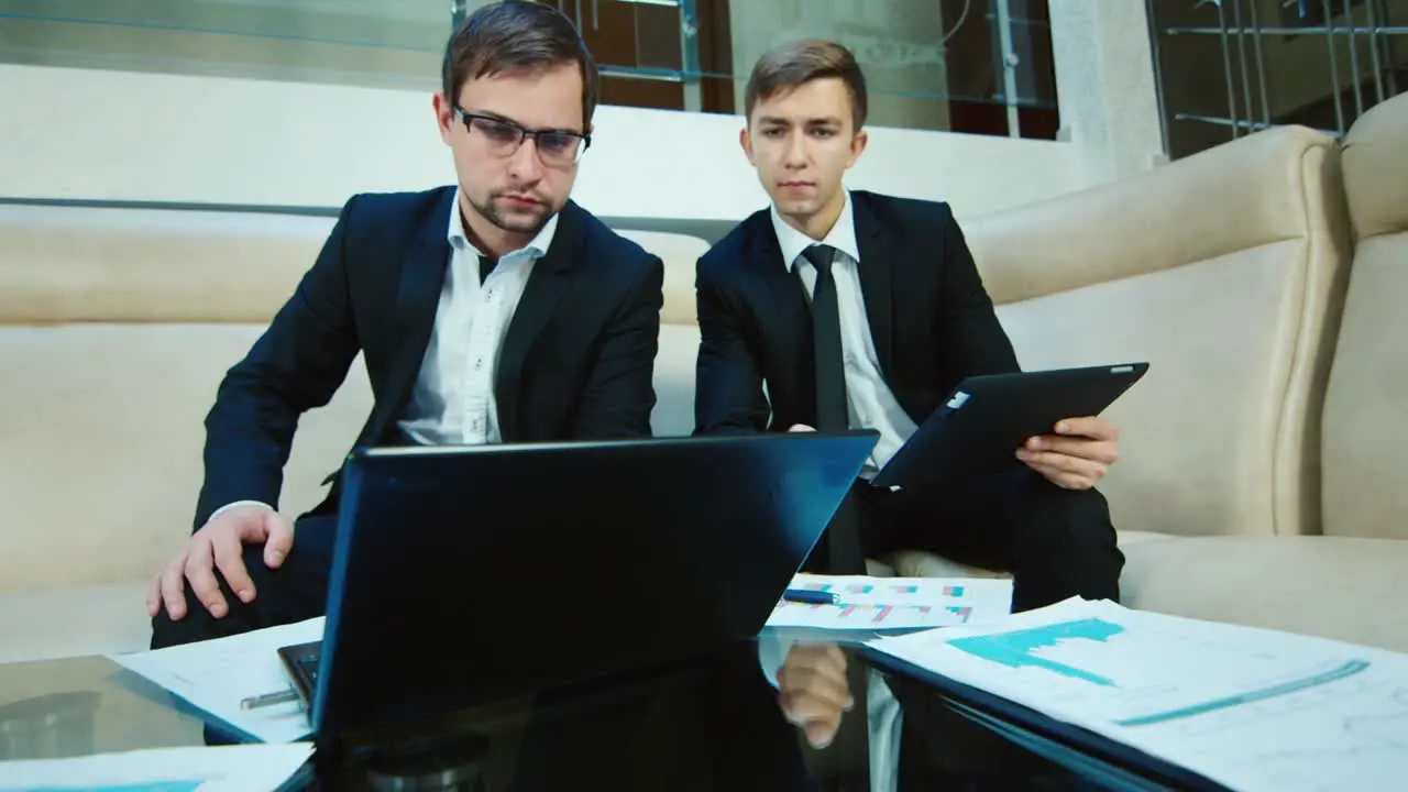 Two businessmen work with documents and a laptop in the lobby of the hotel