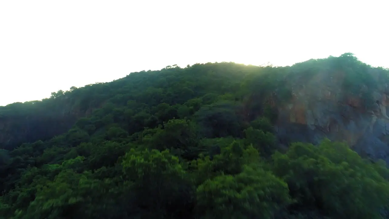 Drone shot flying forwards towards a mountain showing a setting sun and its flare revealing a city below