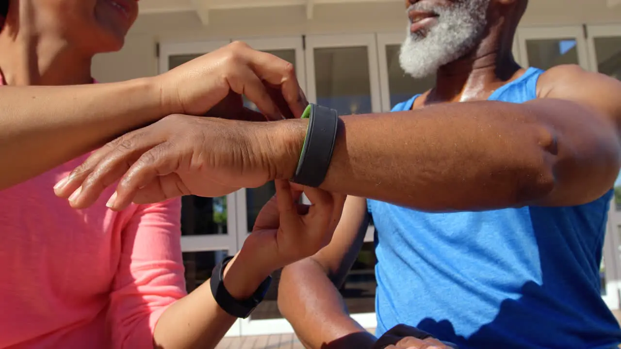 Front view of mature black woman helping man to wear fitness band in back yard of their home 4k