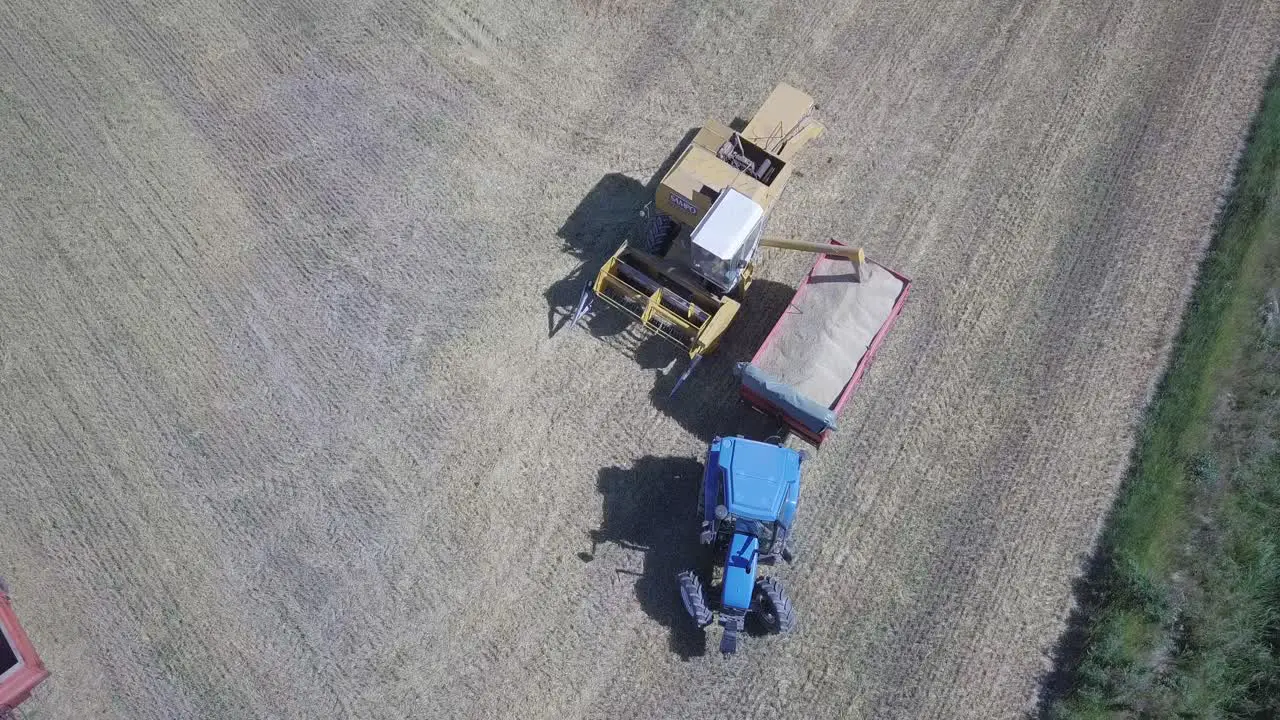 Combine Harvester Unloading Grain tractor trailer carriage aerial top down view