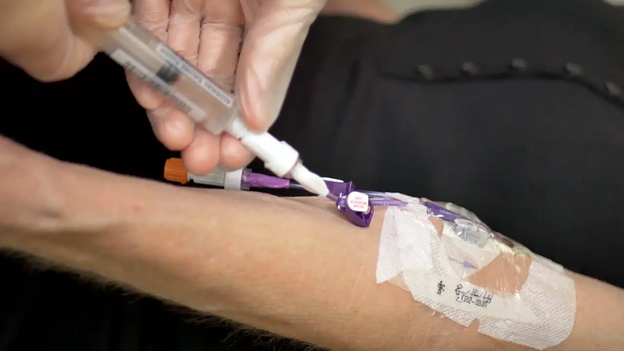 Vertical shot of a medical nurse doing an at home iv patient visit wearing sterile gloves and injecting saline solution into the blood stream through a picc line