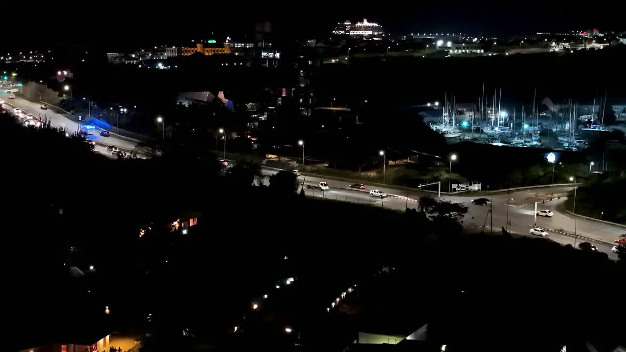 Ambulance with constant blue lights zooms racing past cars on highway above bridge in tropical city at night drone of Curacao