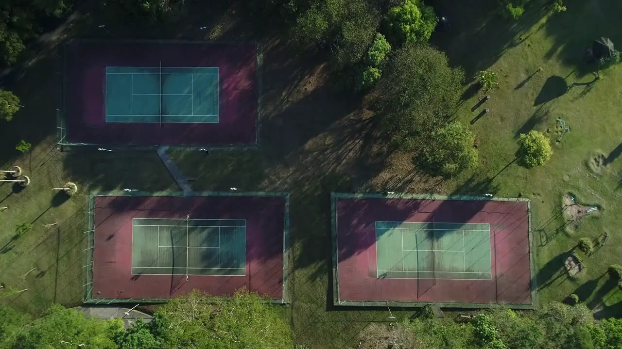 Drone with camera going uphill shows tennis courts with nature around in public park sports health leisure in 4K resolution