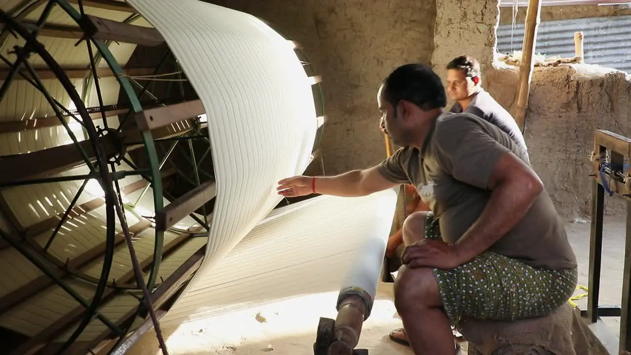 Rural Indian workers weaving cotton in spinning machine inside clay house