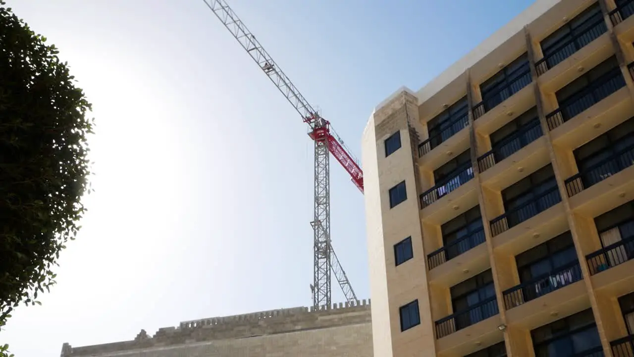 Construction industrial tower crane working near hotel building on windy day in Malta island time lapse view