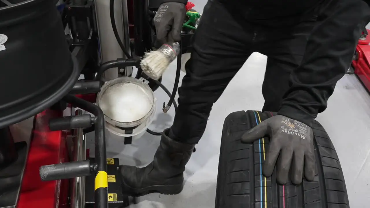 Car mechanic putting tire mounting liquid lube on aluminum alloy wheel prepping it for fixing a tire