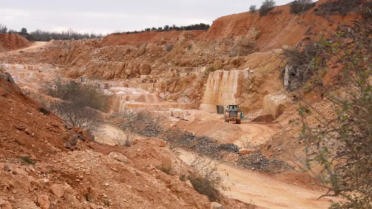 Limestone quarry with loader excavator carrying stone debris Wide handheld shot