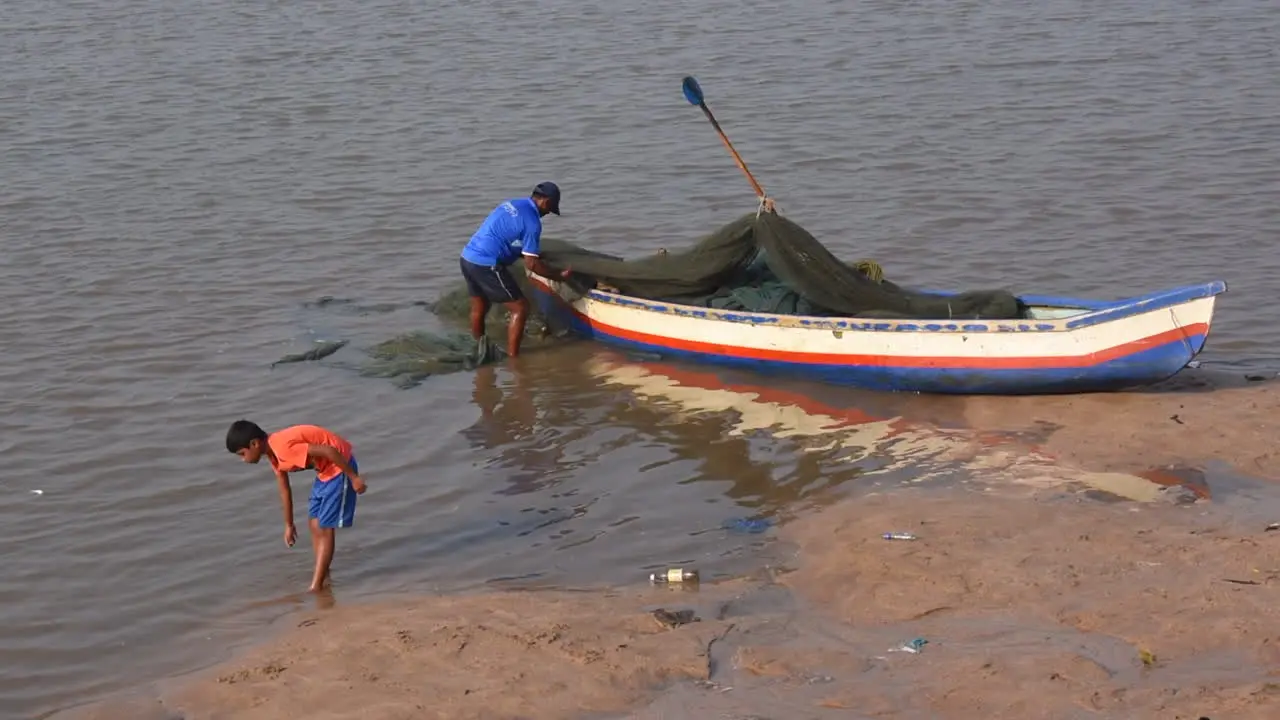 An Indian Fisherman preparing and cleaning his Fishing net and Small fishing boat near a shore before going in to sea for fishing video background in prores 422 HQ