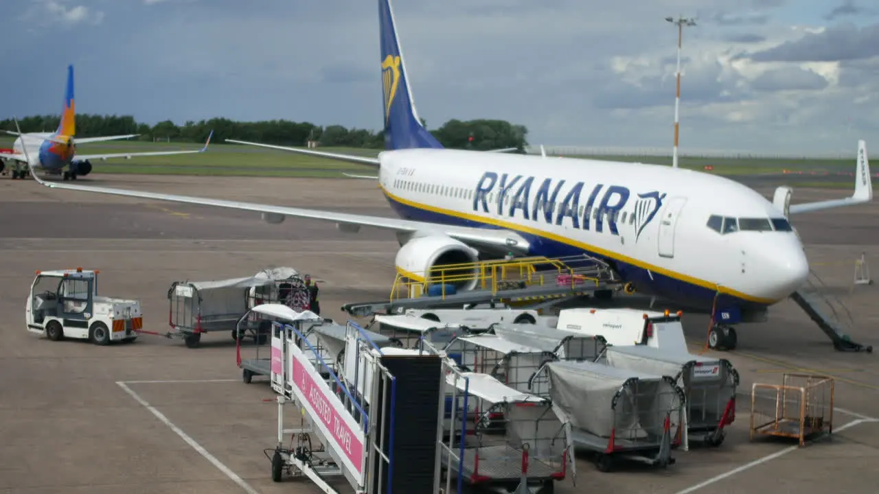 Loading baggage onto a Ryanair plane on the runway with baggage handlers and airliners at the airport