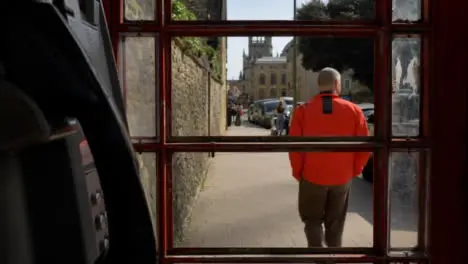 Pedestal Shot Rising Up Behind Old Phone Box as Pedestrian Walks Down Street