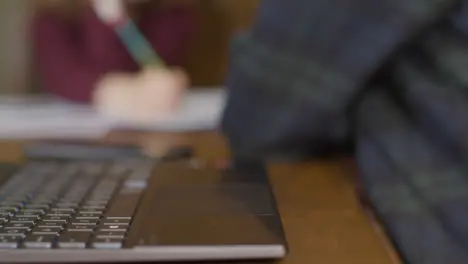 Sliding Close Up Shot of Hands Using Laptop Mouse with Child In Background Doing Homework