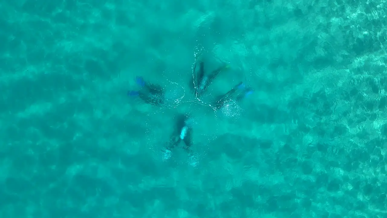 Looking down at four scuba divers underwater with bubbles breaking the ocean surface