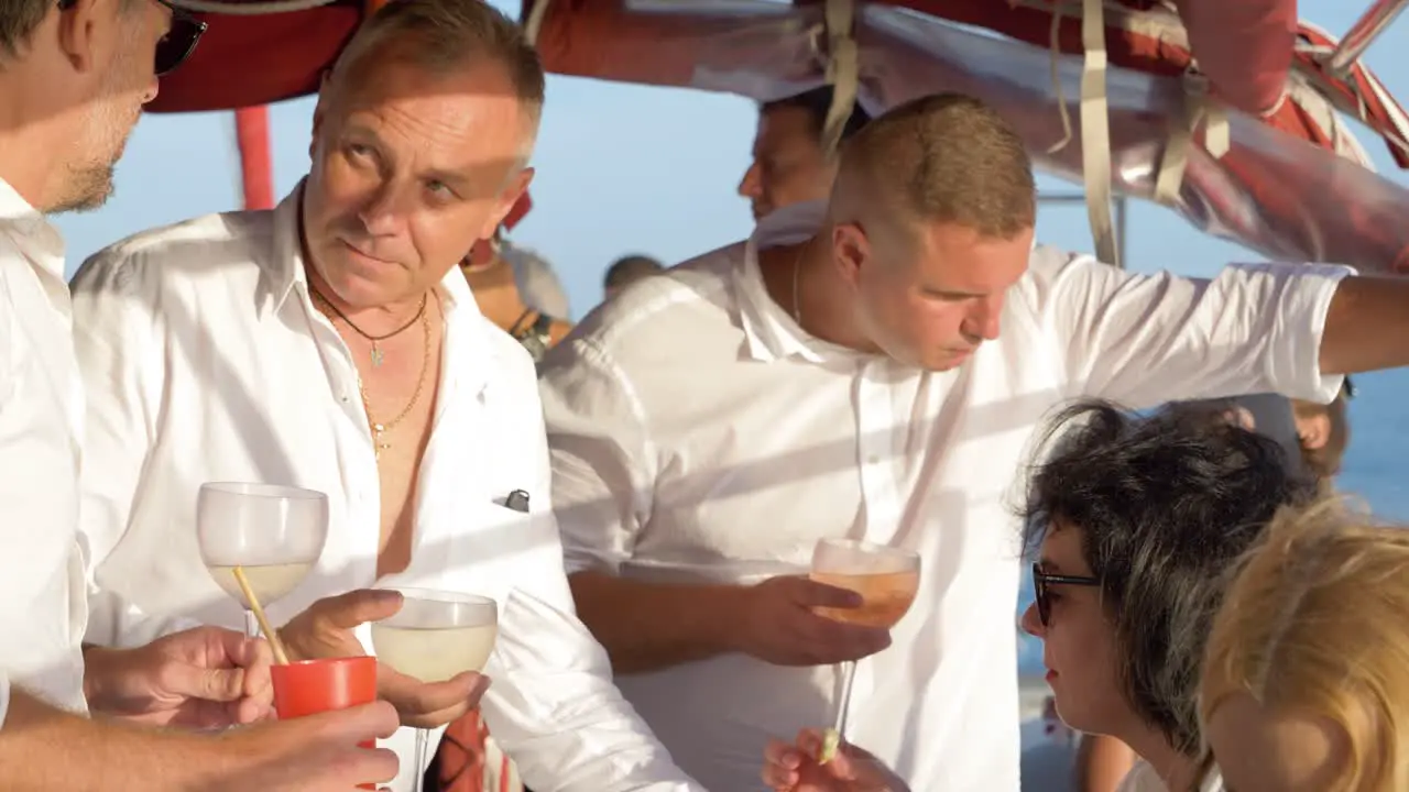 Men and women socialise with each other and enjoying some cocktails on a catamaran sailing boat