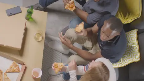 Overhead Shot Of Friends Sitting On Sofa At Home Eating Takeaway Pizza Delivery 