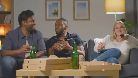 Multi-Cultural Friends Sitting On Sofa At Home Watching TV Eating Takeaway Pizza Delivery 5