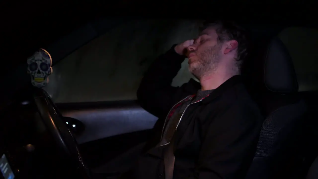 A man sleeping in his car at n ight next to a busy road in a city