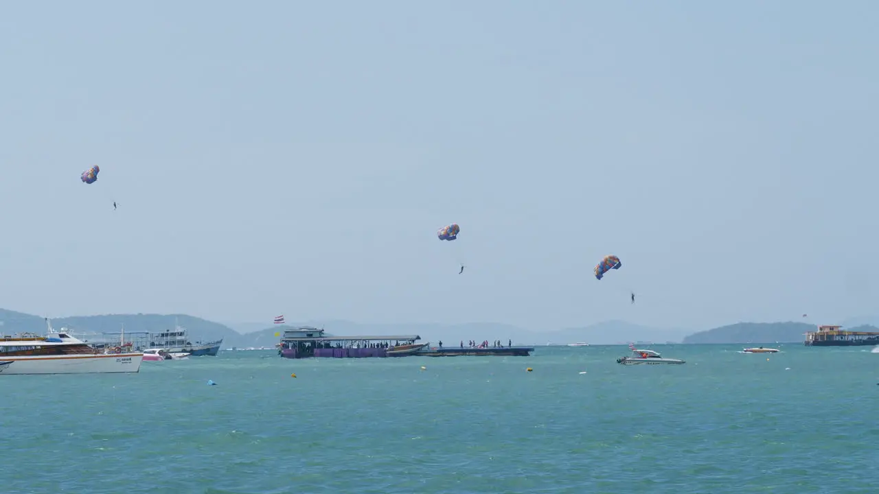 Three people parasailing in Pattaya as they are being pulled by boat to gain altitude while are other boats are seen Thailand