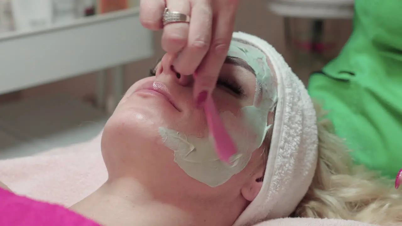 Beautician Applying Facial Mask For Peeling Treatment on Face of Woman in Spa Salon Close Up