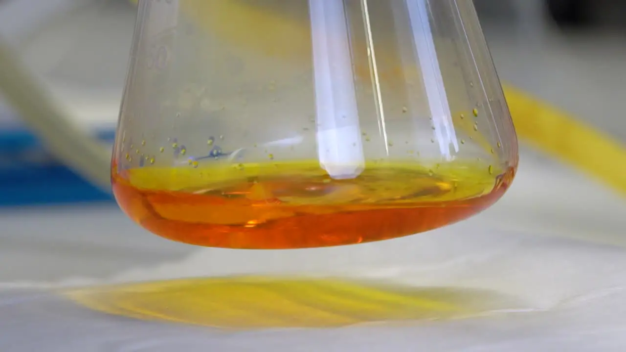 Close-up of orange liquid dripping into a chemistry flask