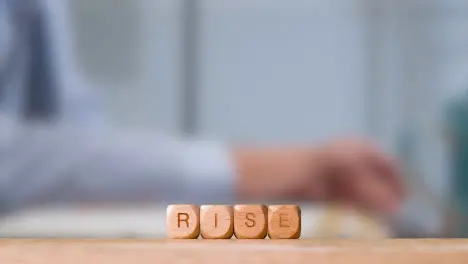 Business Concept Wooden Letter Cubes Or Dice Spelling Rise With Office Person Working At Laptop In Background