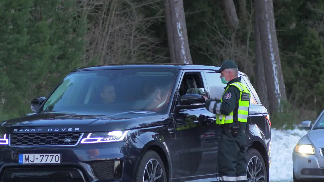 Lithuanian border guard officer control passenger SUV car at the Lithuania Latvia border during crisis measures in the fight against the novel coronavirus Covid-19 medium shot from a distance