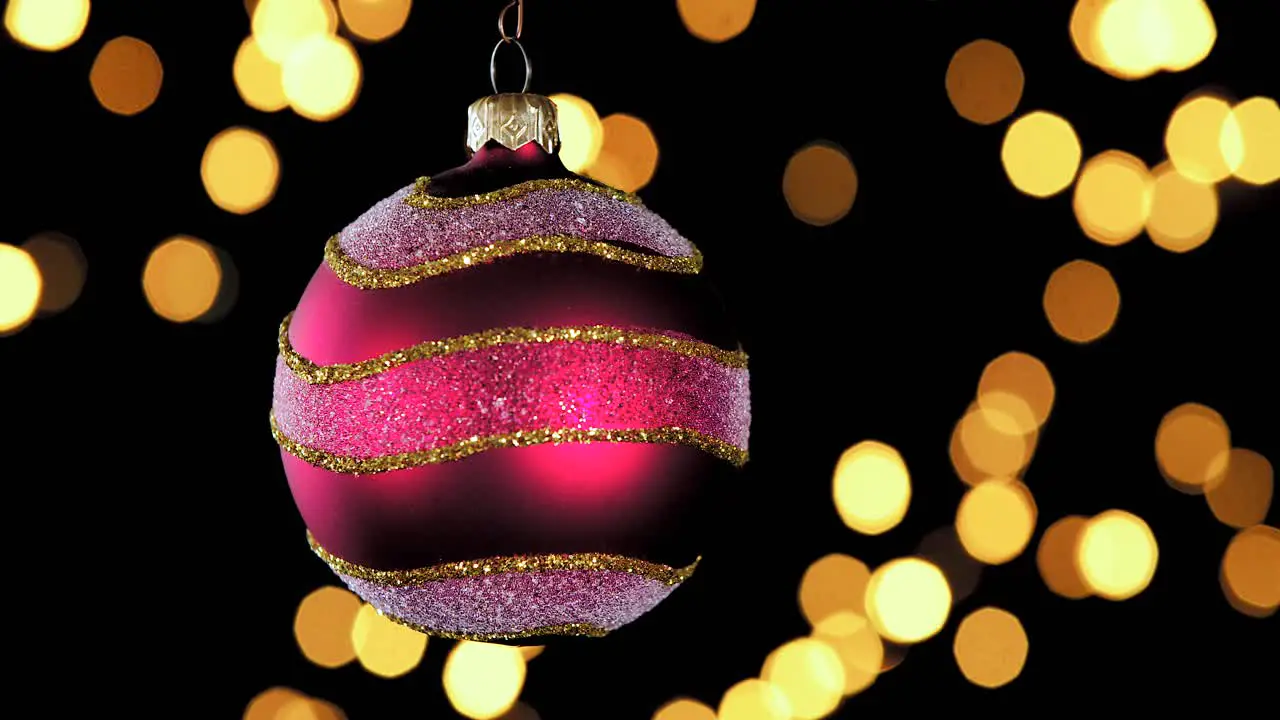 single red Christmas ball ornament with golden silver glitter stripes and out of focus lights flickering in the background close up