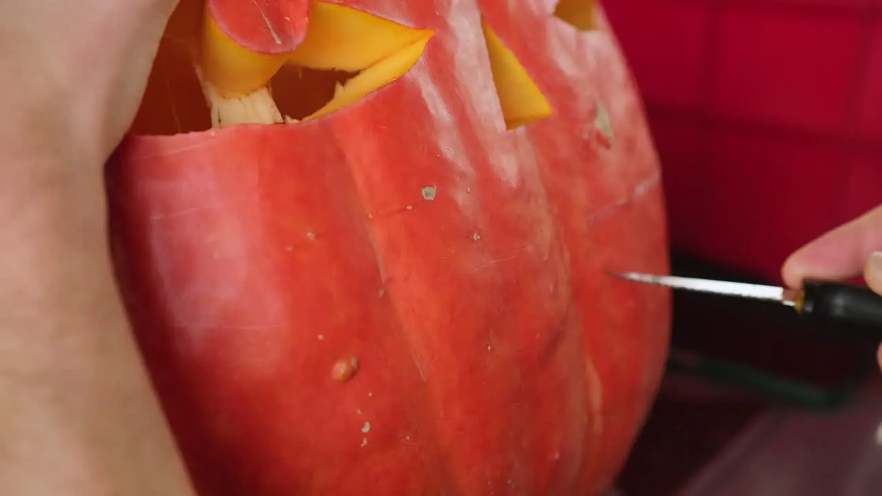 Knife carving a creepy smile on big pumpking for Halloween decoration spooky Jack-o-lantern decor close-up