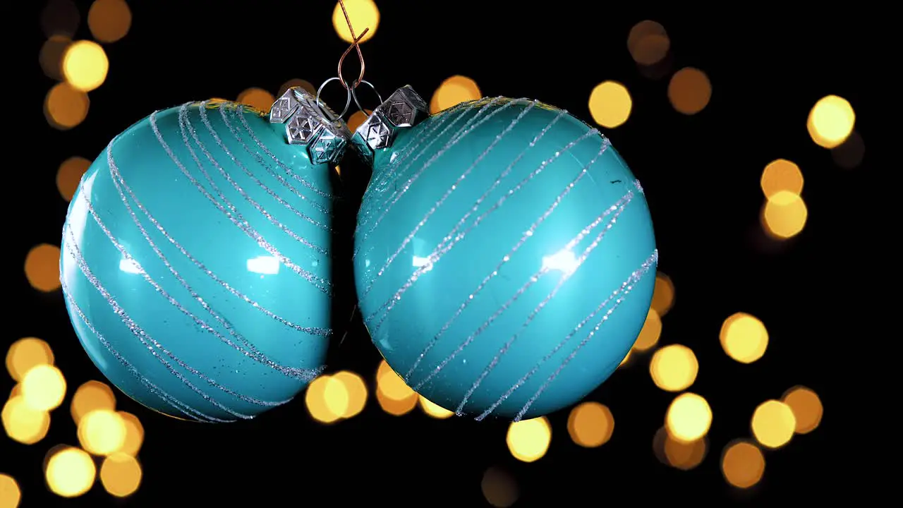 two blue turquoise Christmas ball ornament with glitter stripes and out of focus lights flickering in the background close up