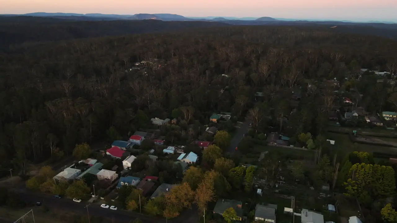 High lowering Drone shot over town with road and traffic surrounded by dense forest bushland