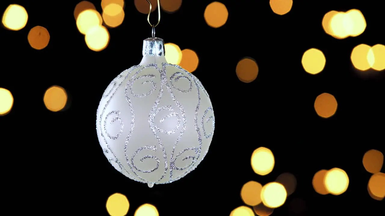 single white Christmas ball ornament with silver glitter stripes and out of focus lights flickering in the background close up