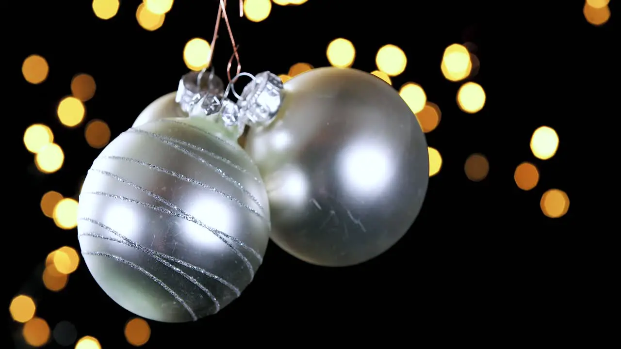 three silver Christmas ball ornaments with out of focus lights flickering in the background close up