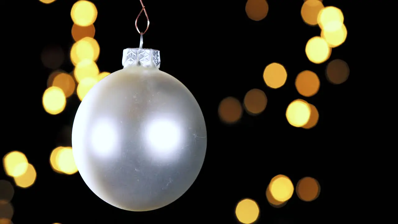 single silver Christmas ball ornament with out of focus lights flickering in the background close up