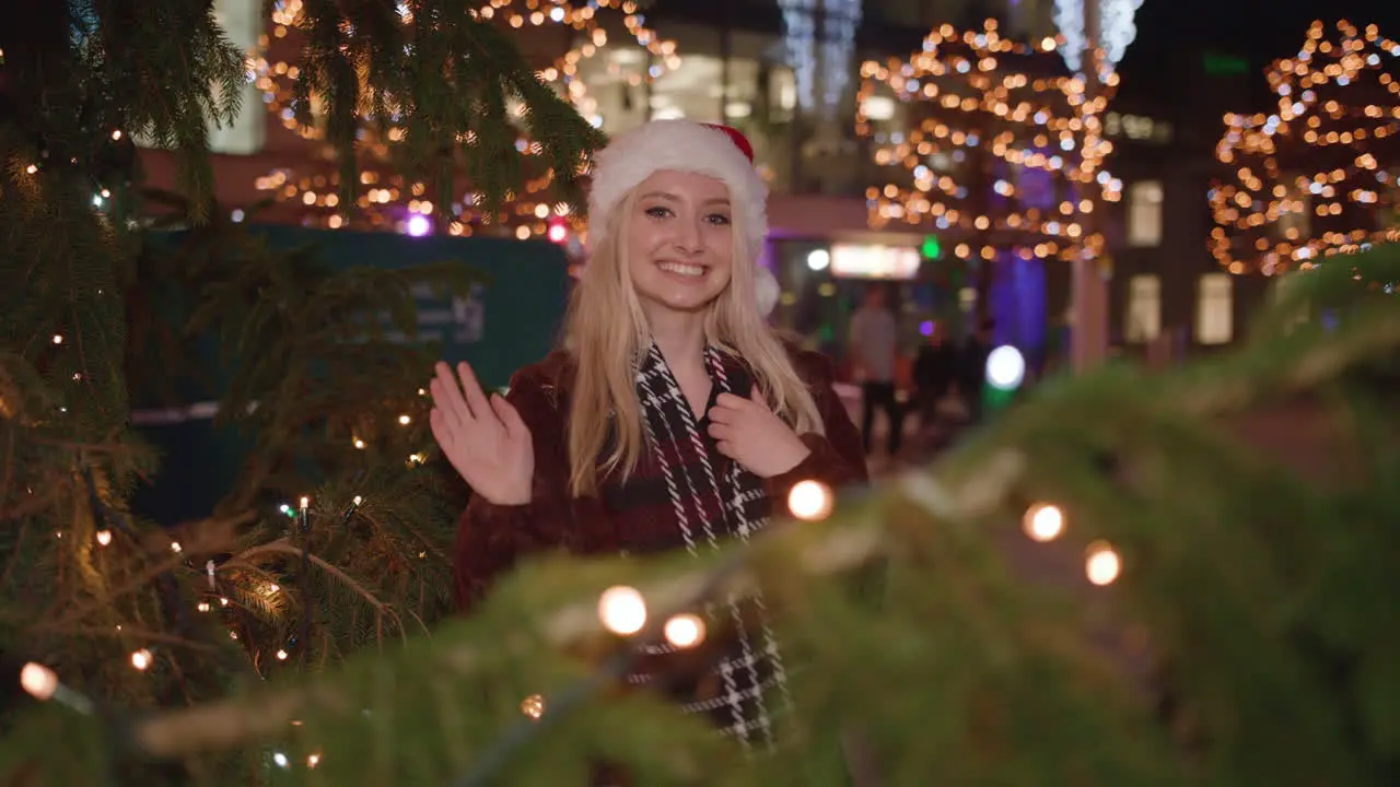 Young woman surprises partner by popping out from behind Christmas tree and smiling