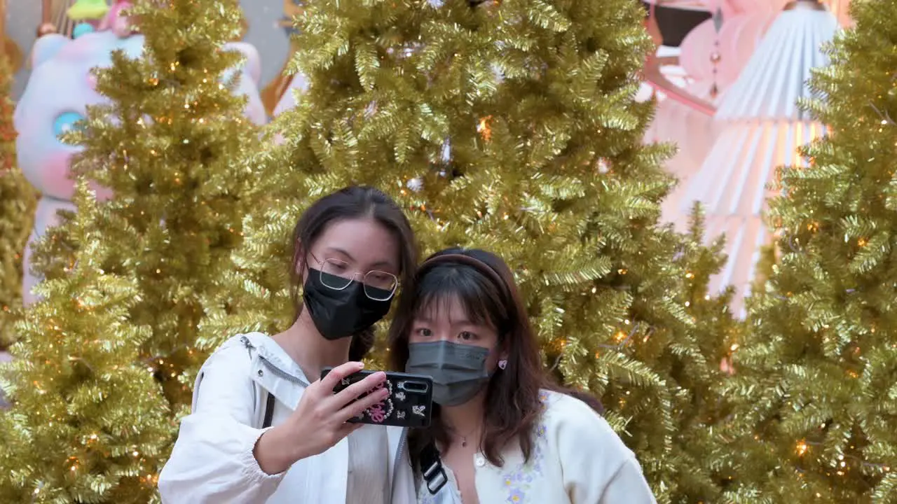 Friends wearing face masks take a selfie with golden Christmas trees in the background as they enjoy their evening at a Christmas theme installation event in Hong Kong