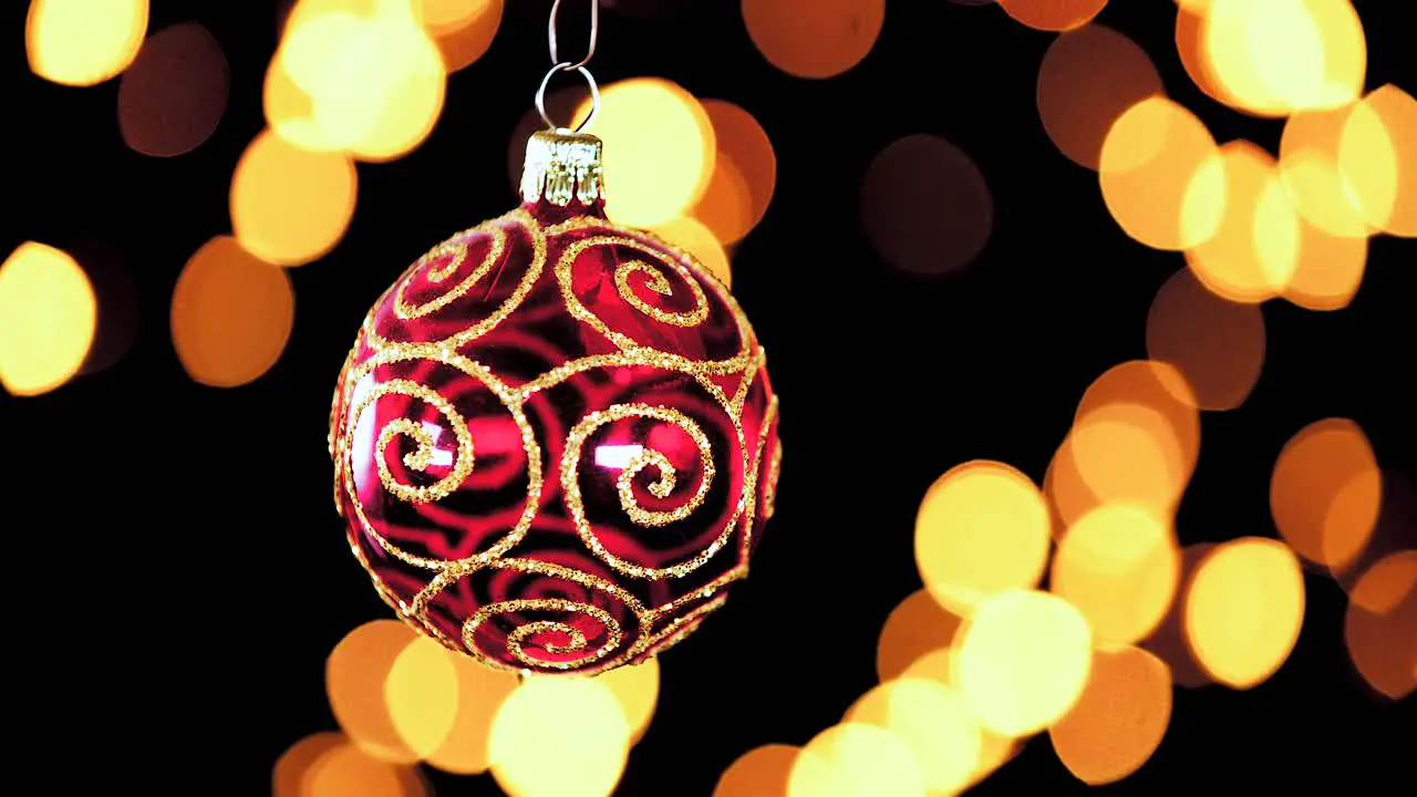 single red clear Christmas ball ornament with golden glitter stripes and out of focus lights flickering in the background close up