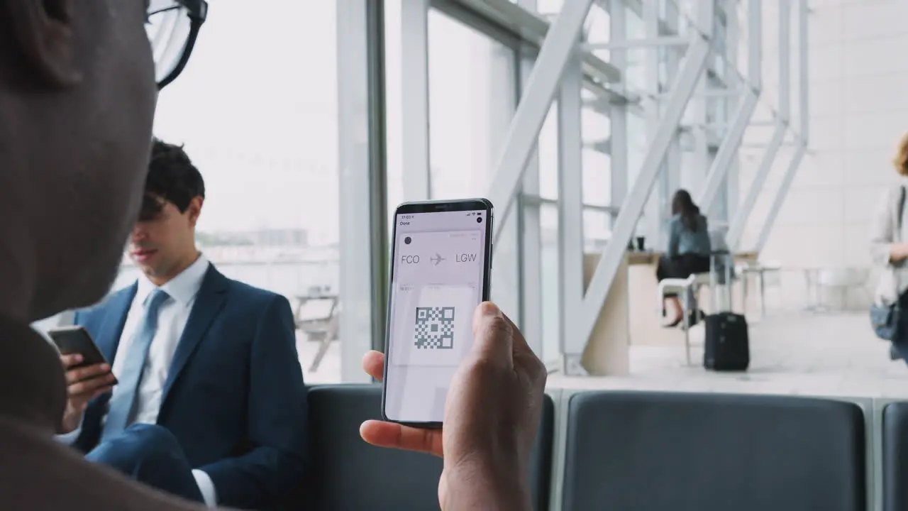 Close Up Of Businessman In Airport Departure Lounge Looking At E-Ticket On Mobile Phone Screen