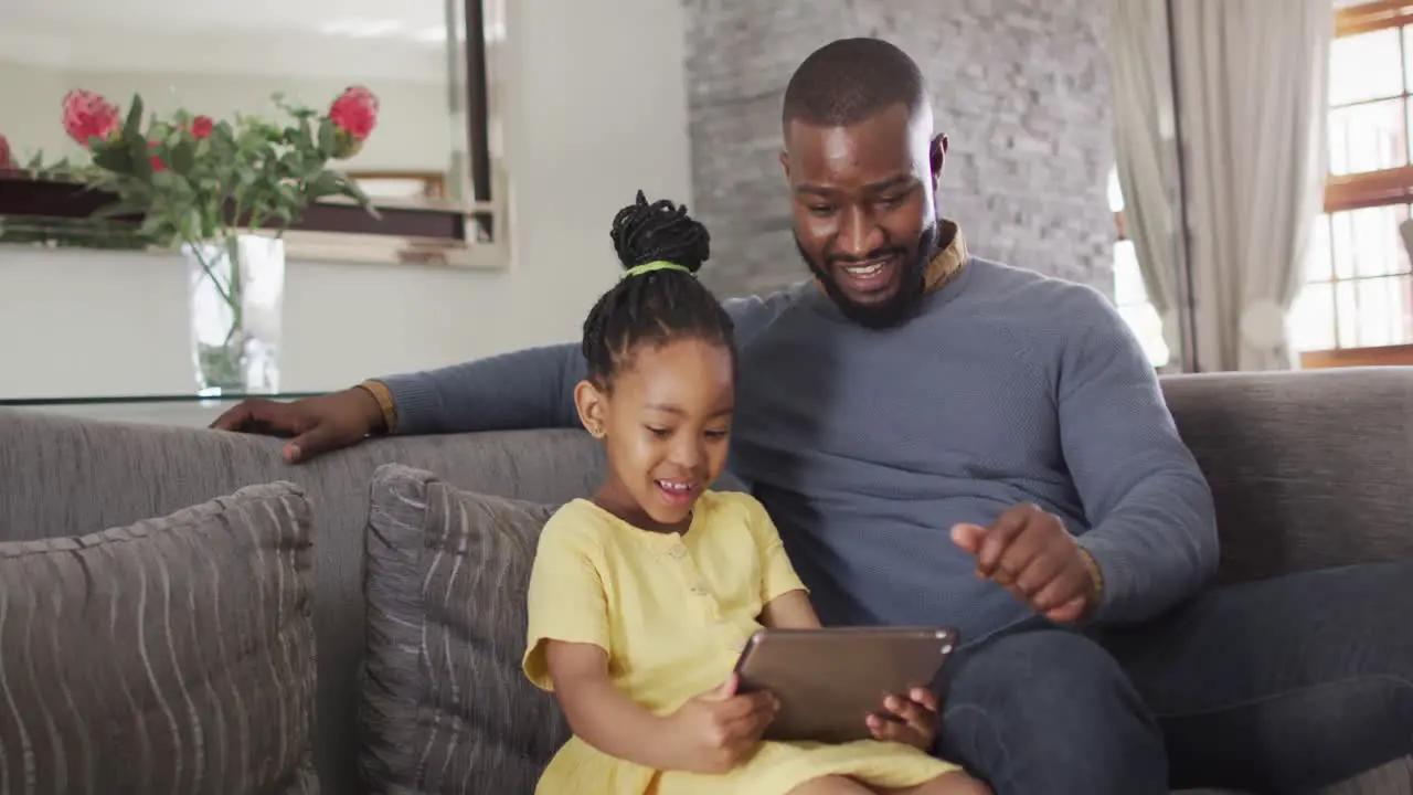 Happy african american daughter and father using tablet on sofa