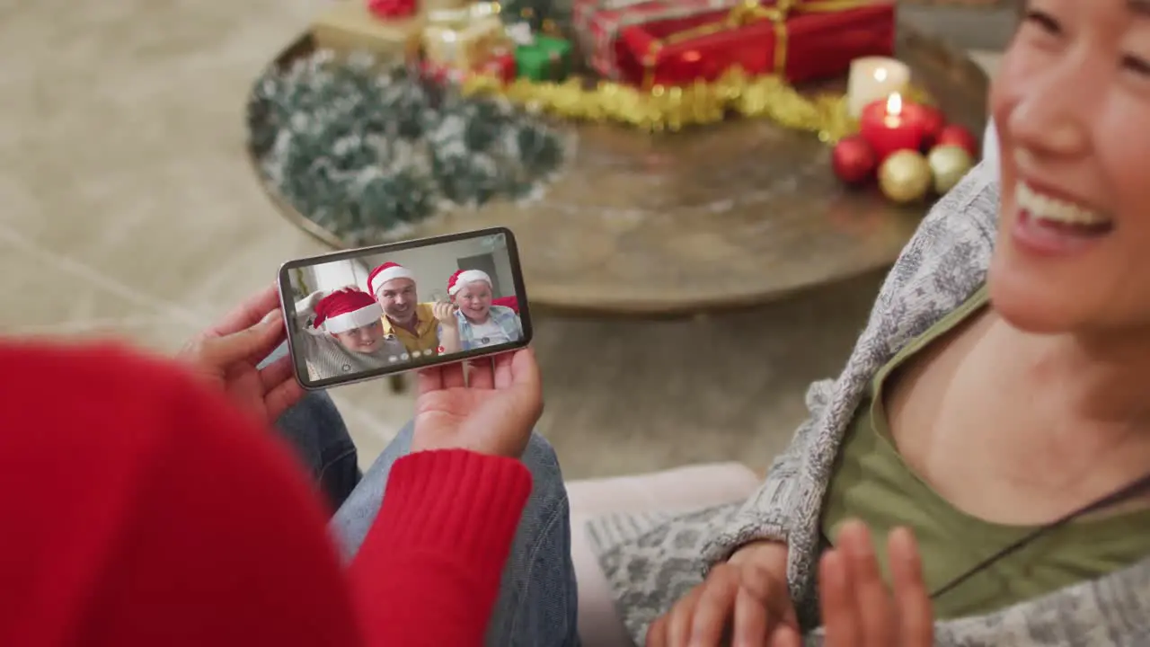 Smiling asian couple using smartphone for christmas video call with happy family on screen