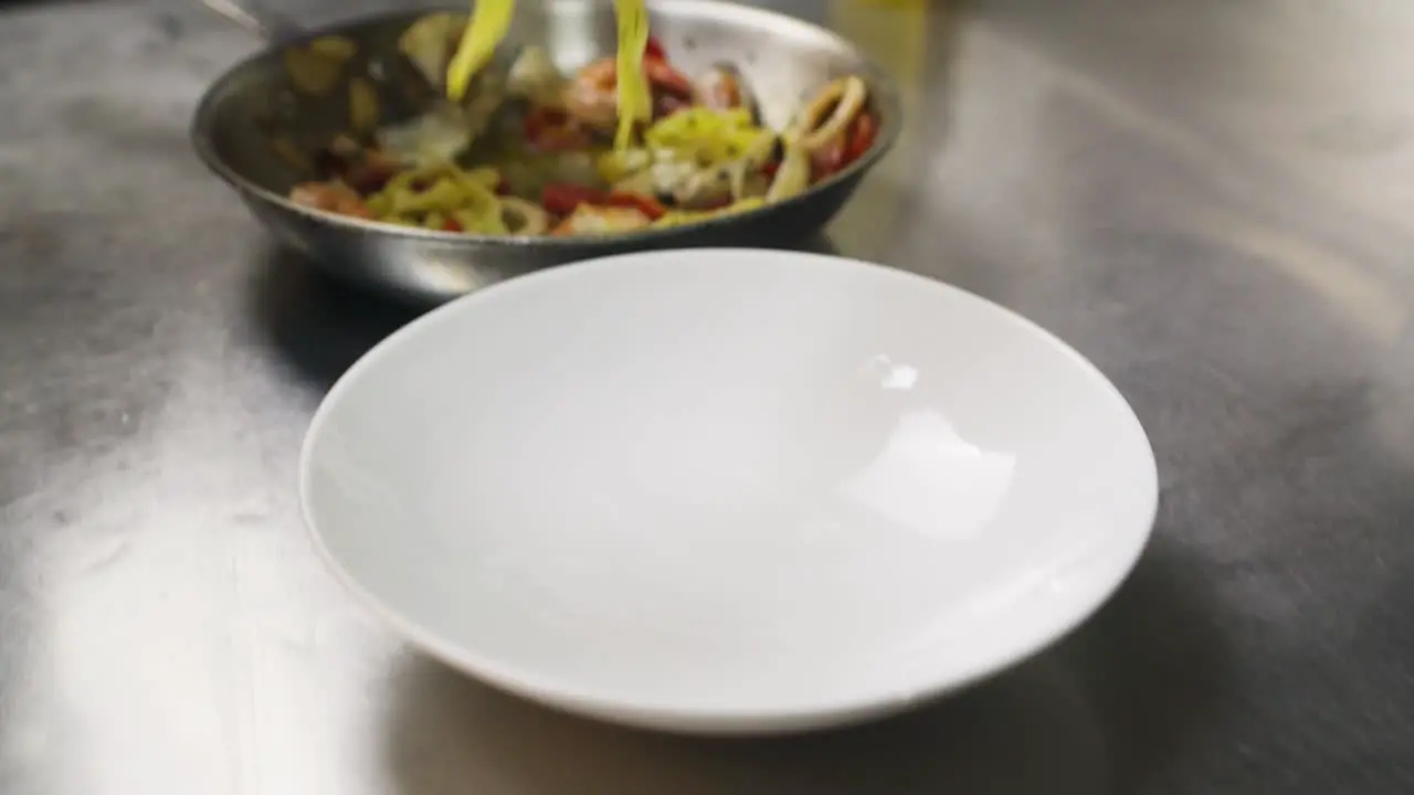 Professional chef close up plate of tagliatelle ai frutti di mare Mediterranean classic dish in a restaurant kitchen