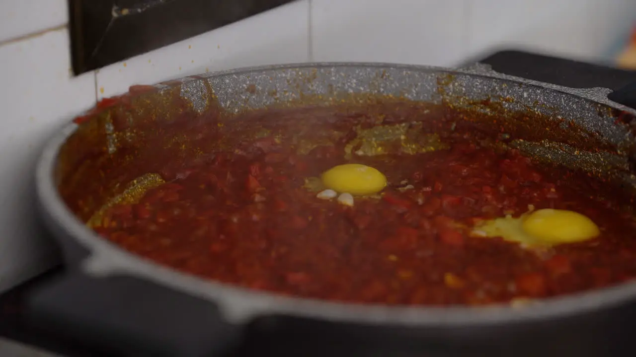 man breaks an egg into a bubbling tomato sauce preparation of homemade Shakshouka filmed in natural day light