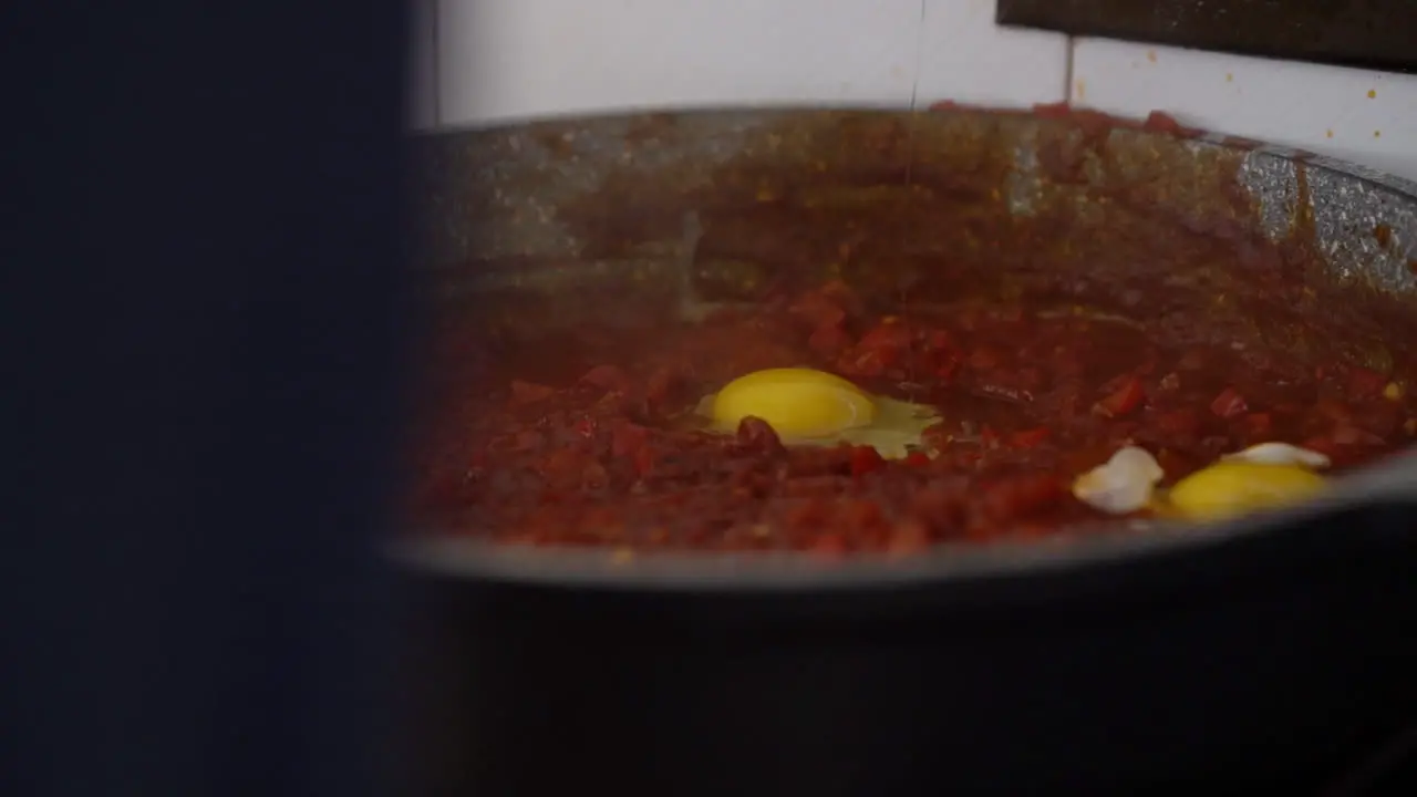 man breaks an egg into a bubbling tomato sauce preparation of homemade Shakshouka filmed in slow motion and natural day light