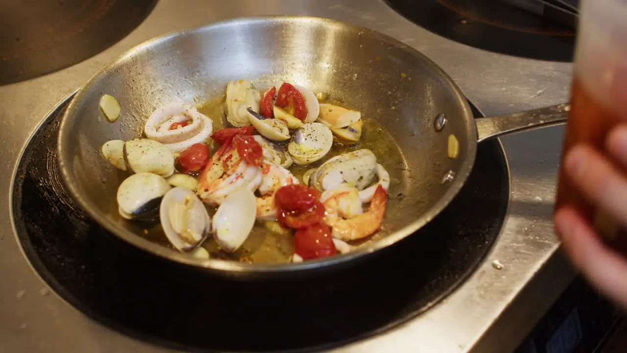 Mediterranean seafood dish preparation in professional restaurant kitchen chef add red fresh cherry tomatoes in a pot