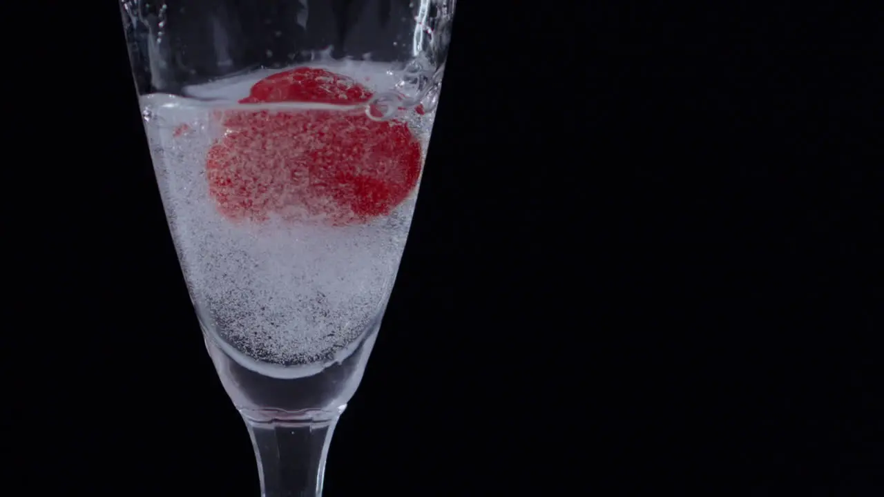 Slowmotion shot of a frozen Raspberry falling into a glass of clear water