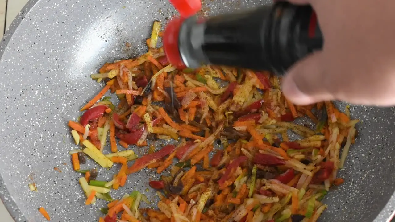 Man's hand adding soy sauce to frying vegetables in a wok